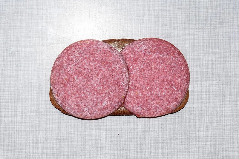 Top shot of a slice of bread smeared with margarine and topped with salami on a white Resopal plate