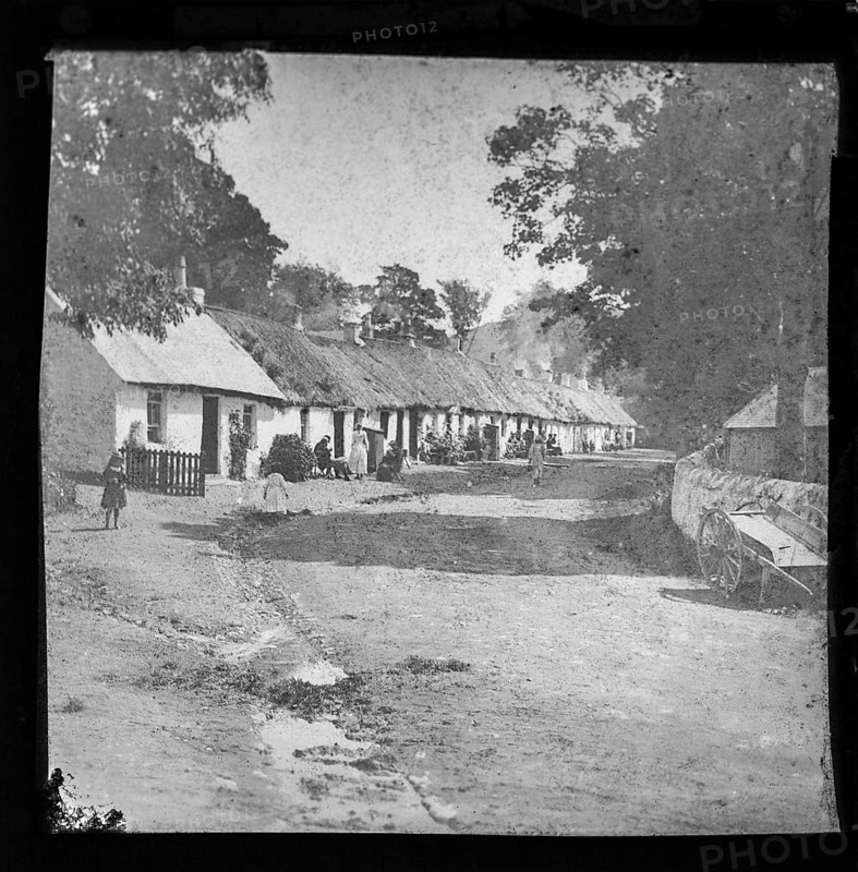 Prosperous looking people sitting outside thatched workers' one storey whitewashed cottages, possibly tourists to the Lake District, England, UK late 1800s c 1900