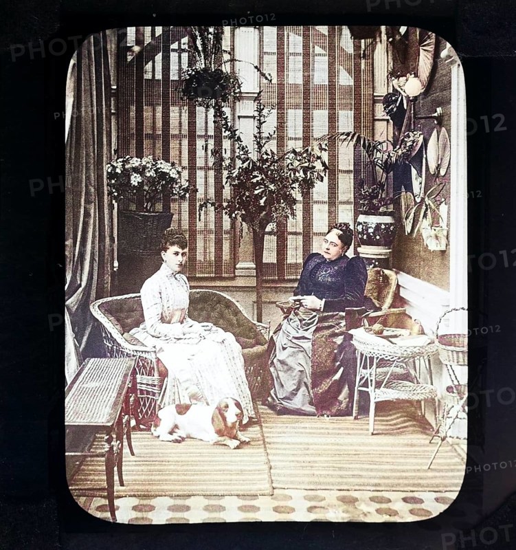 A colourised magic lantern slide of Queen Mary, when Princess May of Teck, with her mother, the Duchess of Teck, formerly Princess Mary of Cambridge, indoors in conservatory room, Victorian period, Britain, UK c 1890-1900