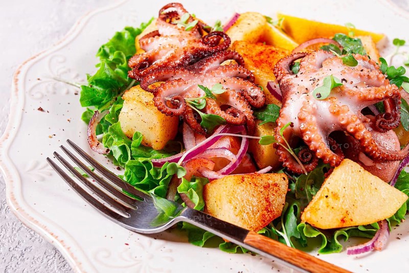 Grilled octopus with baked potatoes and fresh herbs, on a decorative light plate, homemade, no people