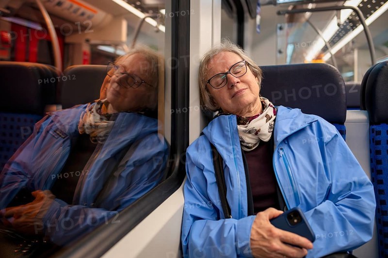 Innenaufnahme, ältere Frau, Brille, sitzt in S-Bahn, Zug, schläft, erschöpft, träumt, Smartphone, Handy, Spiegelung, abends, nachts, Nachtaufnahme, ÖPNV, Nahverkehr, Stuttgart, Baden-Württemberg, Deutschland