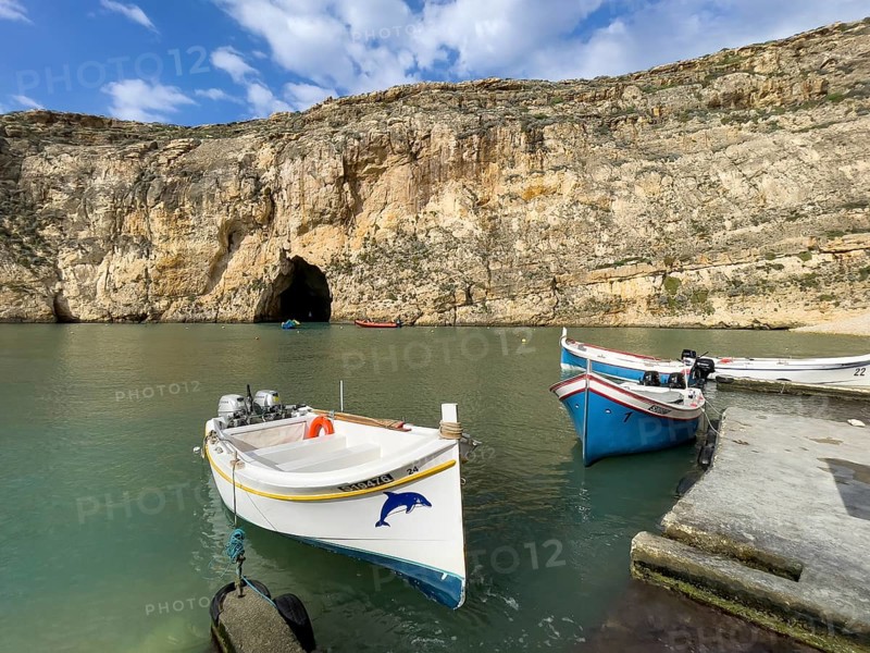 Moored excursion boat without tourists in inland sea of Gozo, in the background tunnel from passage through rock face to open sea, island of Gozo, Malta