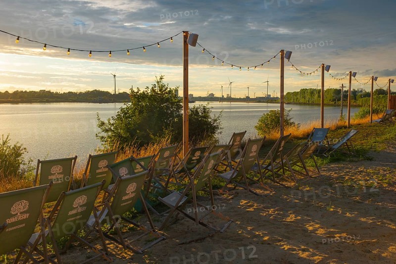 View from the outdoor area of a restaurant at Lankenauer Höft over deckchairs through a string of lights onto Neustadt harbour in the evening light, Weser, Bremen, Germany