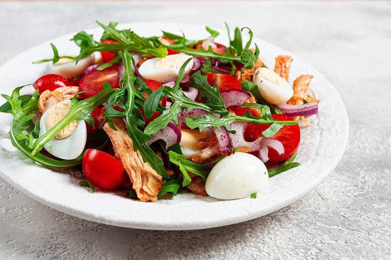 A warm salad with fried chicken fillet, arugula and cherry tomatoes, and boiled quail eggs, on a white plate, no people