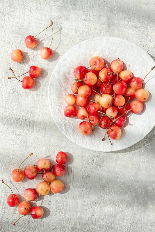 Yellow cherries on a white platter, scattered on the table, natural light, top view