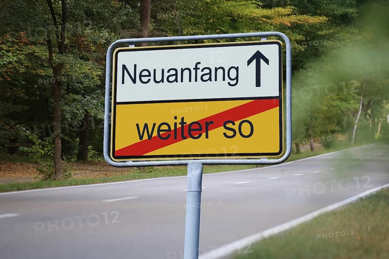 (Photomontage) An exit sign in front of a country road points in the direction of NEUANFANG and leaves WEITER SO