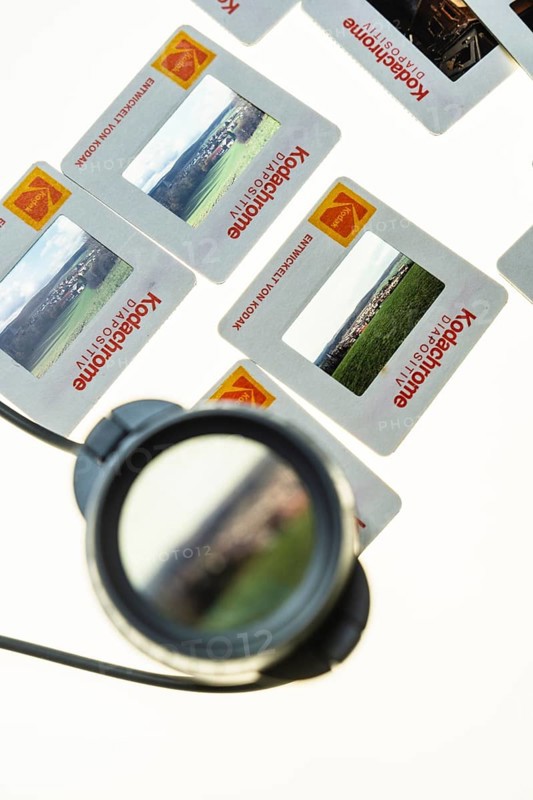 Many framed Kodachrome slides on a light table with magnifying glass, top shot
