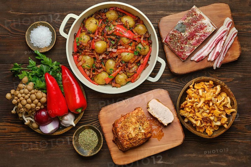 Organic ingredients on a rustic wooden countertop, showcasing a hearty meal preparation with fresh vegetables, pork meat, bacon mushroom and herbs
