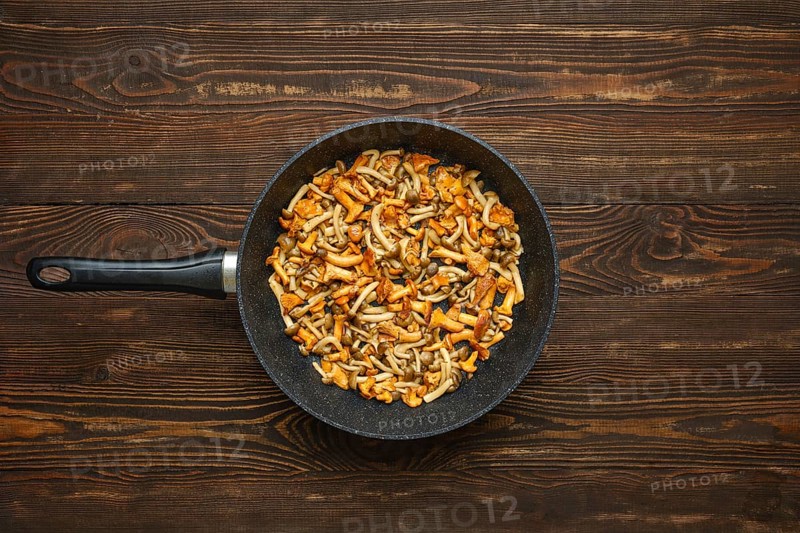 A vibrant mix of fried chanterelles and honey mushrooms in a pan on a wooden table. The colourful dish showcases a blend of textures and flavours of forest mushrooms