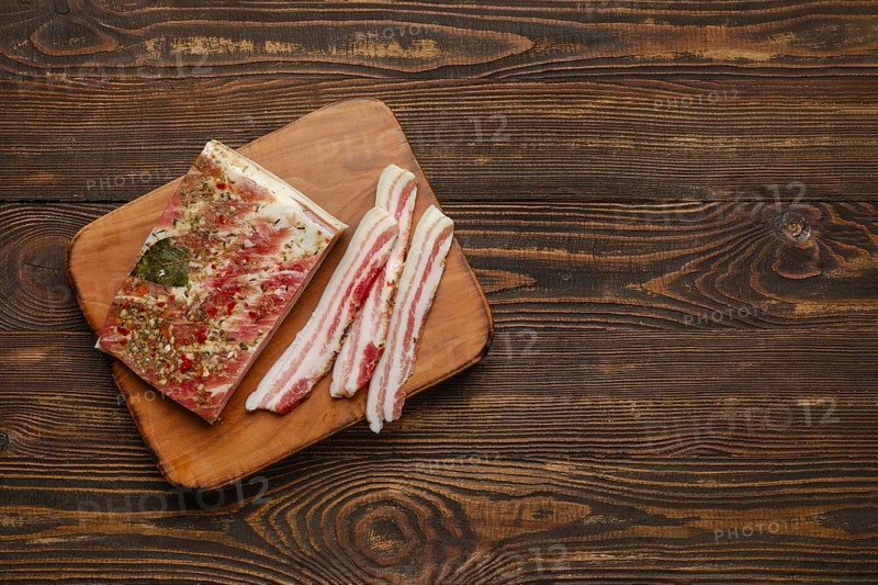 Thick slices of seasoned bacon on a wooden cutting board, showcasing a blend of herbs and spices