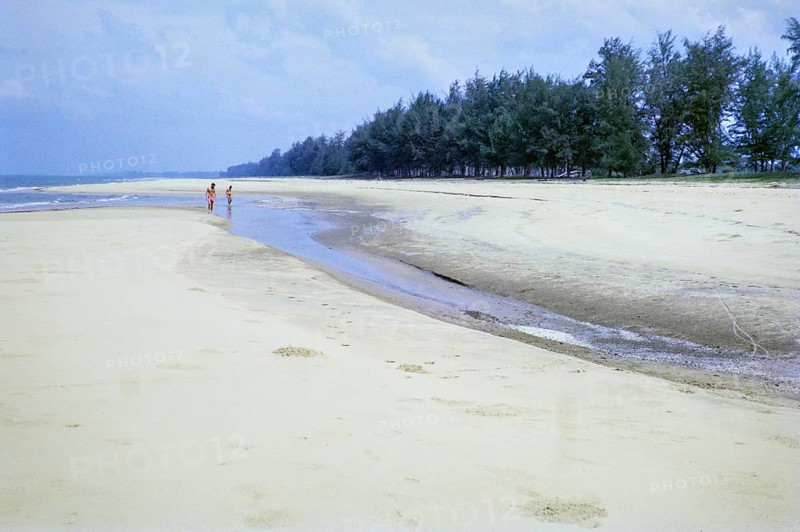 Men walking on sandy beach south of estuary, Rompin, East coast, Pahang, Malaya, Malaysia, south east Asia 1964