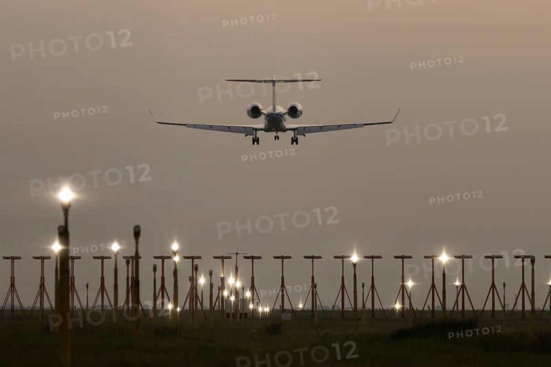 Executive business jet passenger aircraft landing over runway lights at sunset, London Stansted airport, Essex, England, United Kingdom
