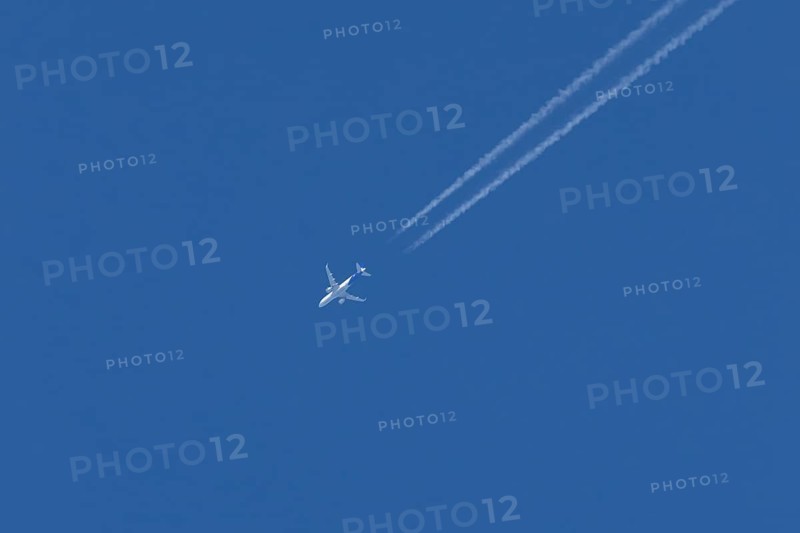 Jet passenger aircraft with a vapour trail or contrail flying in a blue sky, England, United Kingdom