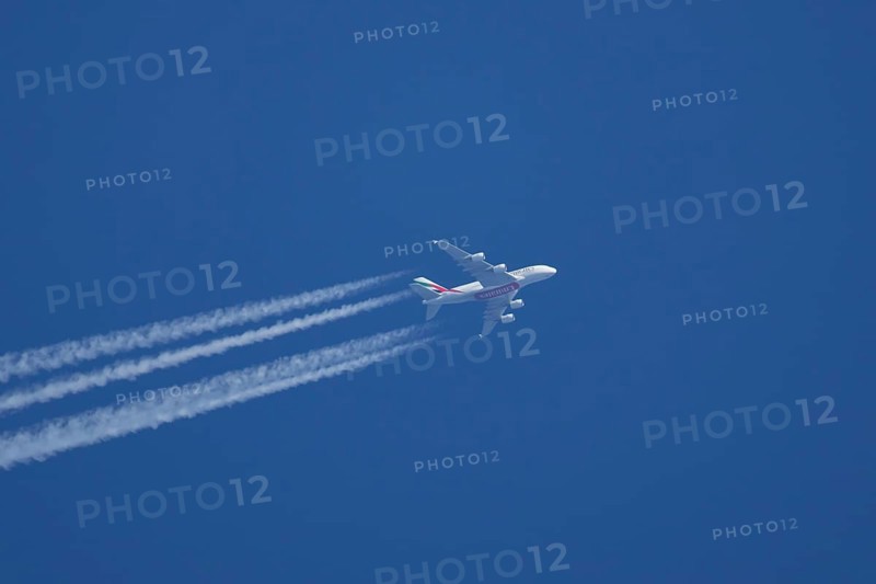 Airbus A380 jet passenger aircraft of Emirates airlines flying with vapour trails or contrails behind in a blue sky, England, United Kingdom