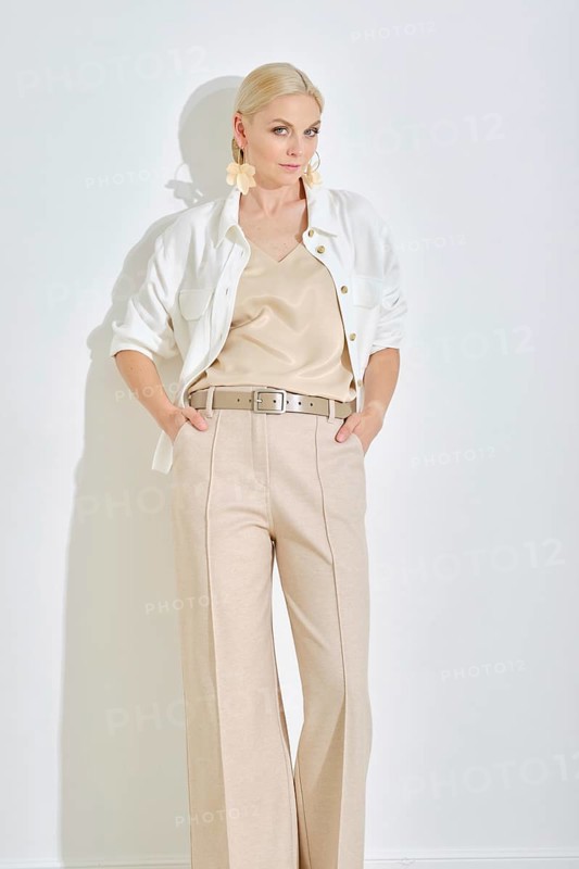 A model showcases a chic outfit featuring a light-colored top and tailored trousers, complemented by a buttoned jacket