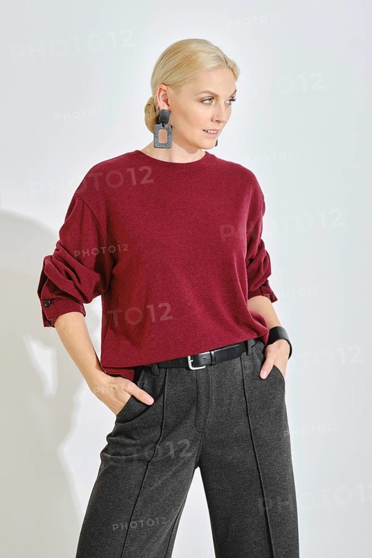 A model stands confidently in a cozy oversized red sweater and tailored dark gray trousers. Her chic look is accentuated with statement earrings, reflecting a contemporary fashion vibe