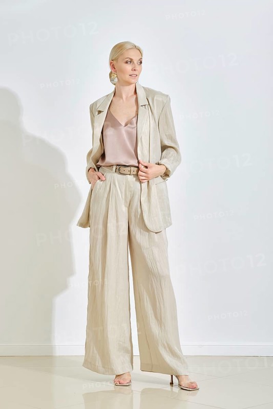 A model showcases a stylish light-colored suit paired with a silk top in a contemporary indoor environment