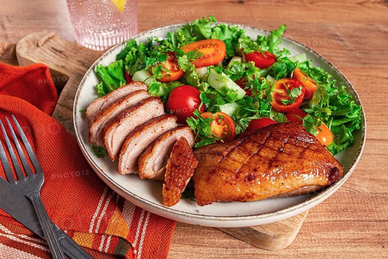 Delicious grilled duck breast served with fresh garden salad and cherry tomatoes at a rustic dining table