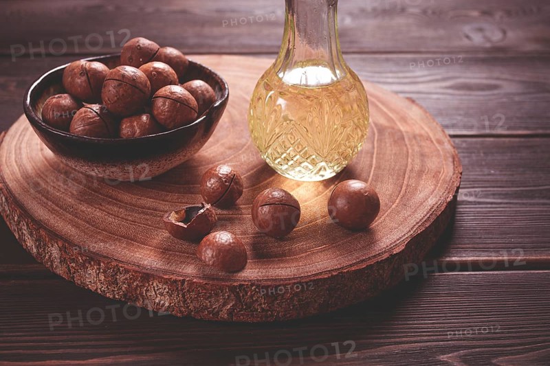 Bottle of macadamia oil, on a wooden board, with macadamia nuts, wooden background, selective focus, no people