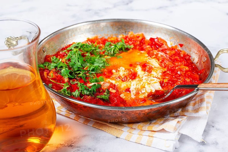 Traditional Turkish dish, scrambled eggs with tomatoes, Menemen, with herbs, in a frying pan, close-up, no people