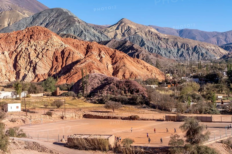 Young people playing football, with coloured hills in the background, erosion, Purmamarca, Jujuy, Argentina