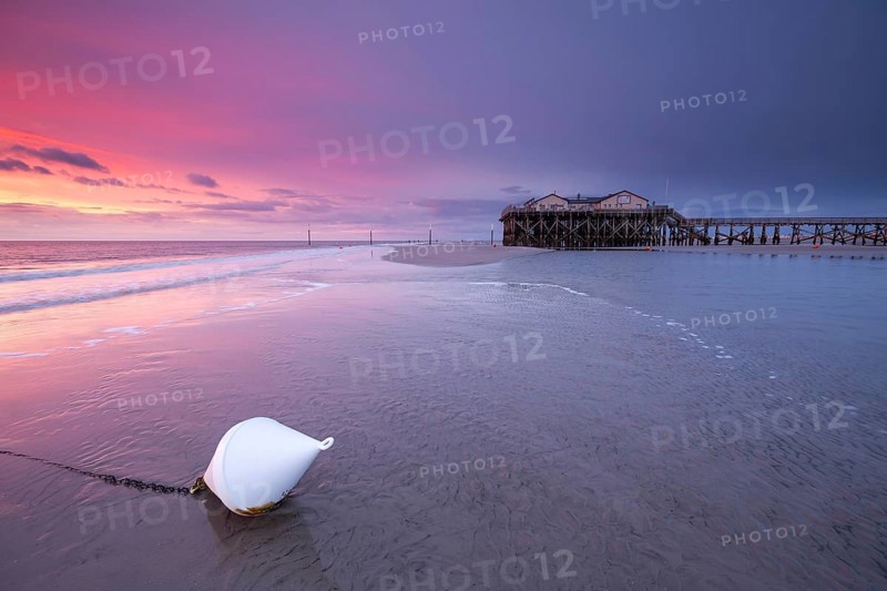 Pile dwellings in St. Peter-Ording in front of the surf in the bright red evening light by the sea