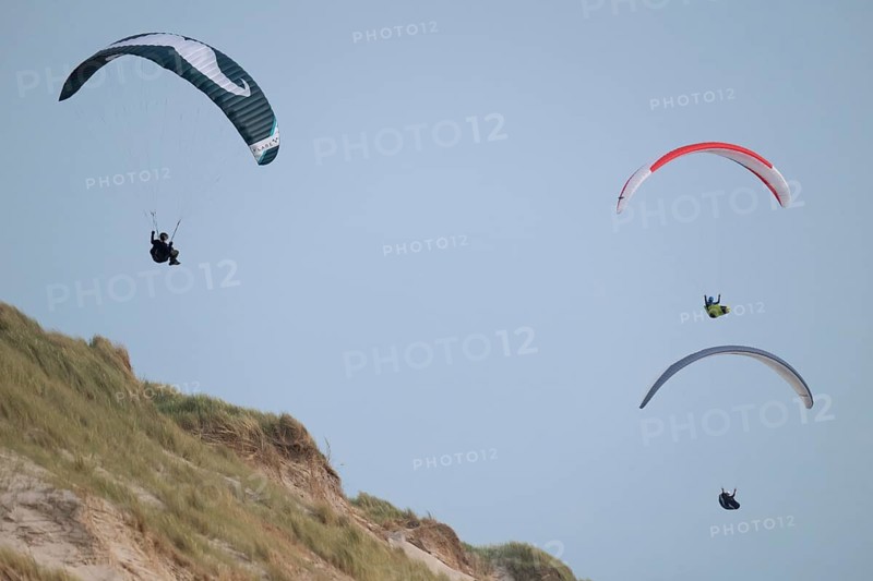 Three paragliders or paragliders in front of a blue sky over a dune landscape, near Hvide Sande, North Sea, Denmark