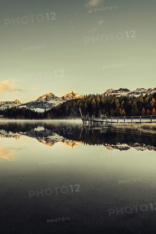 Lake Staz near Sankt Moritz in the Engadin in Switzerland. Morning atmosphere with fog in autumn. Water reflection and snow-covered mountains in the background