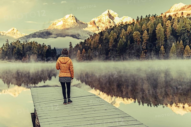 Young woman at Lake Staz near Sankt Moritz in the Engadine in Switzerland. Morning atmosphere with fog in autumn. Reflection of water
