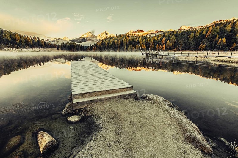Lake Staz near Sankt Moritz in the Engadin in Switzerland. Morning atmosphere with fog in autumn. Water reflection and snow-covered mountains in the background