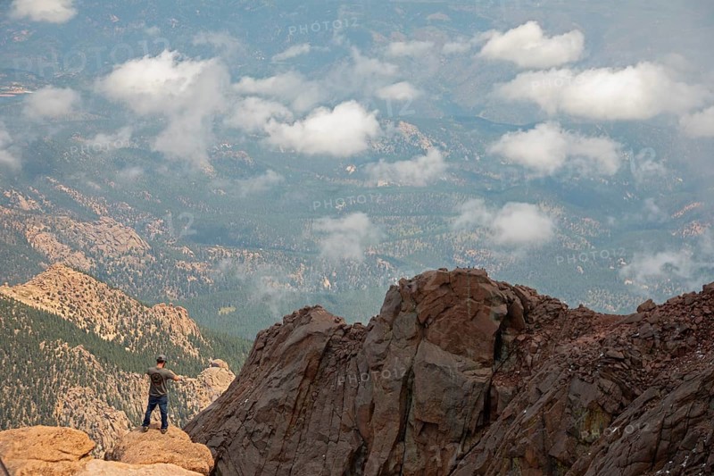 Colorado Springs, Colorado - A man takes photos from the rocks just below the summit of Pikes Peak, a 14, 115' mountain in Colorado's front range. Thousands of tourists visit, most by driving a steep road to the summit, or riding on a cog railway