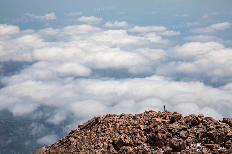 Colorado Springs, Colorado - A man stands on the rocks just below the summit of Pikes Peak, a 14, 115' mountain in Colorado's front range. Thousands of tourists visit, most by driving a steep road to the summit, or riding on a cog railway