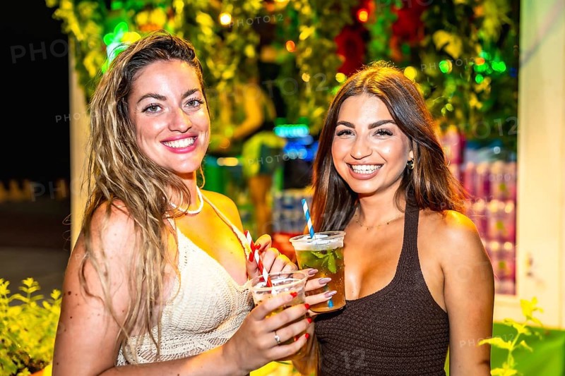 Two beautiful women enjoying cocktails at a summer night party, celebrating and having fun together