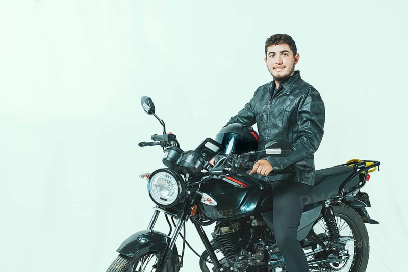 Smiling motorcyclist sitting on his motorcycle holding helmet, isolated. Portrait of handsome biker on motorcycle on isolated background