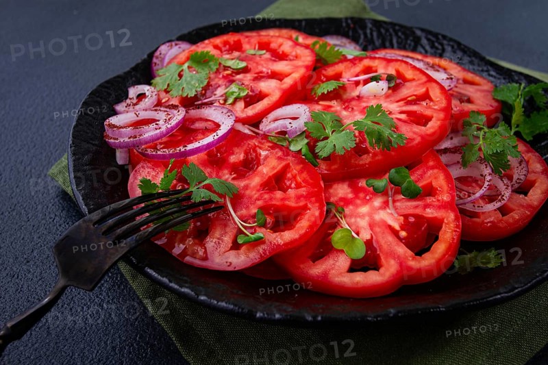 Freshly sliced tomatoes and red onions, garnished with herbs, on a black plate, summer salad, no people