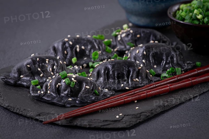 Japanese gyoza dumplings, made of black dough, black gyoza, with green onions and sauce, on a plate, close-up