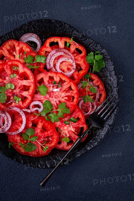 Freshly sliced tomatoes and red onions, garnished with herbs, on a black plate, summer salad, no people