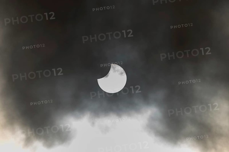 A partial solar eclipse occurs when the moon eclipses part of the sun and is surrounded by dynamic cloud formations. The event takes place during the day and offers an impressive visual experience. High Rhine, Vosges, Great East, France