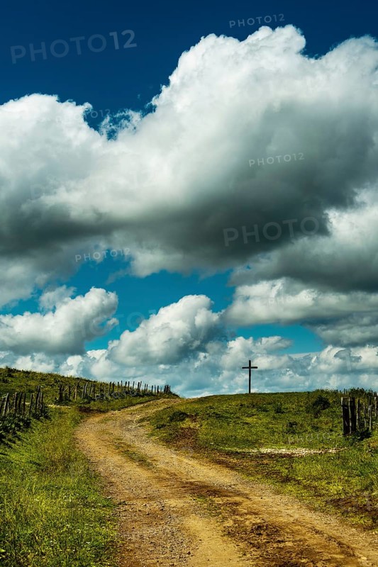 A winding dirt road leads the eye to a solitary cross. Cézallier, Auvergne Volcanoes Regional Natural Park, Puy-de-Dôme, Auvergne Rhone Alpes, France