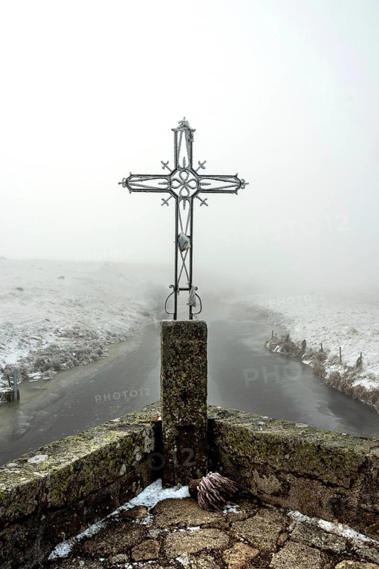 In winter, the Croix du Pont de Marchastel stands proudly amidst a foggy landscape on the Aubrac plateau in Lozere, Occitanie, France