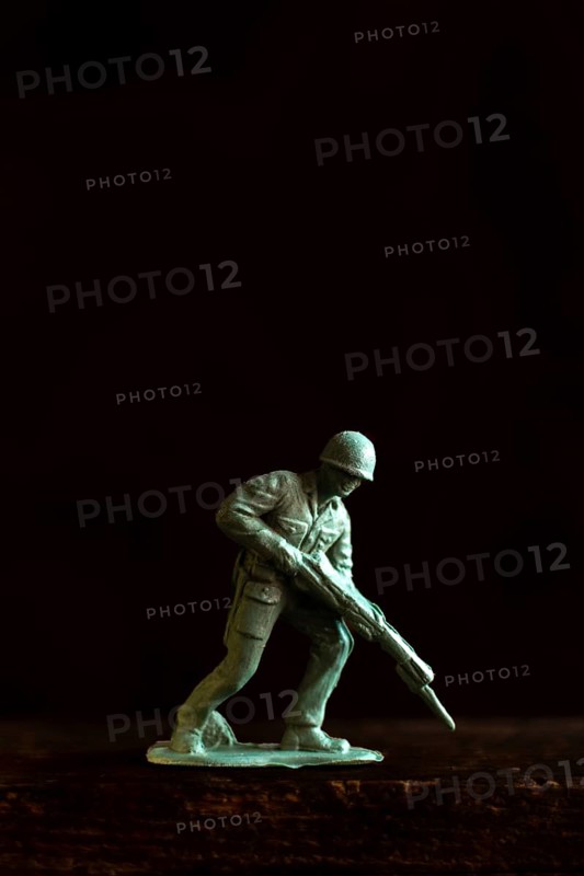 A small soldier figure stands ready with a rifle, capturing the essence of military readiness and attention to detail against a dark backdrop