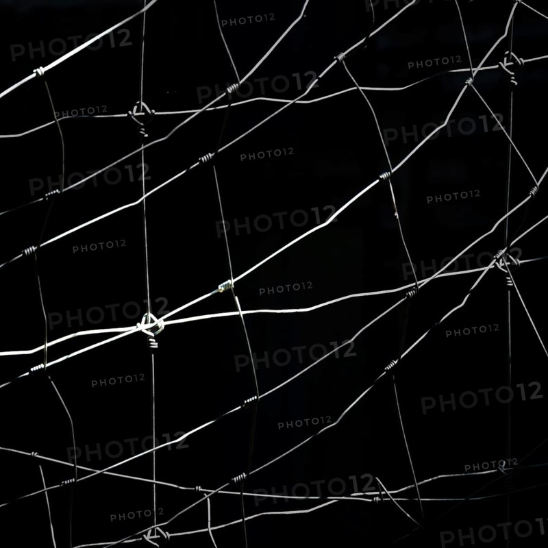 Worn netting stretches across a dark backdrop, showcasing intricate patterns and textures. The play of light and shadow emphasizes the delicate details of the material, creating depth