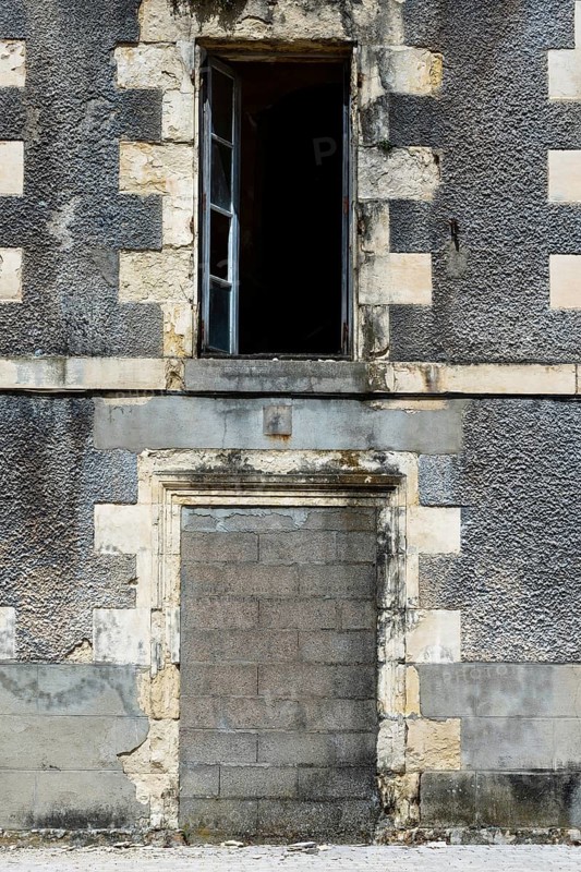 An abandoned structure stands with a weathered gray facade and an open window, highlighting urban neglect in a serene area. The building bears the marks of time and disrepair. France
