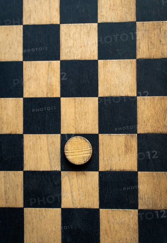 A close-up view of a checkerboard made of black and natural wood squares featuring one wooden piece placed at the center, emphasizing an ongoing game strategy