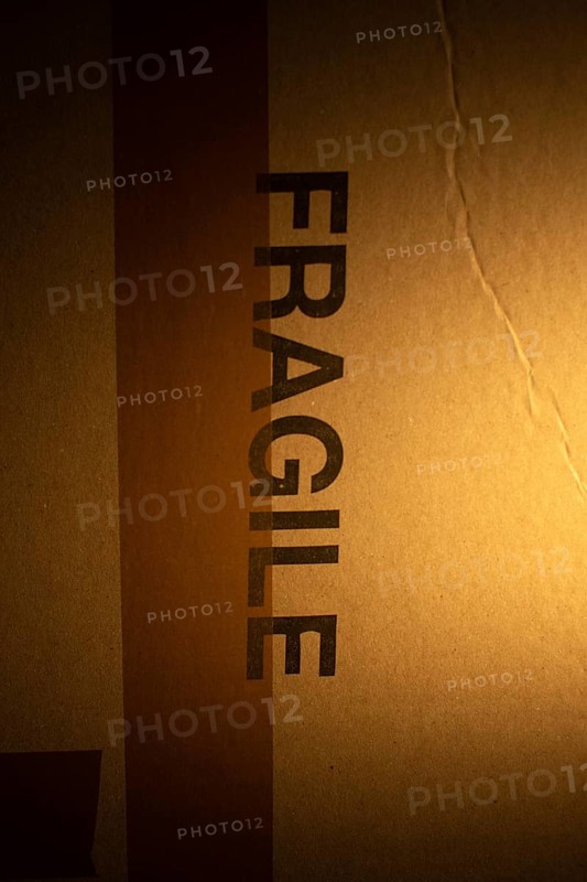 A cardboard package with a clear warning label indicating fragile contents is softly illuminated, emphasizing the need for careful handling due to potential delicate items inside