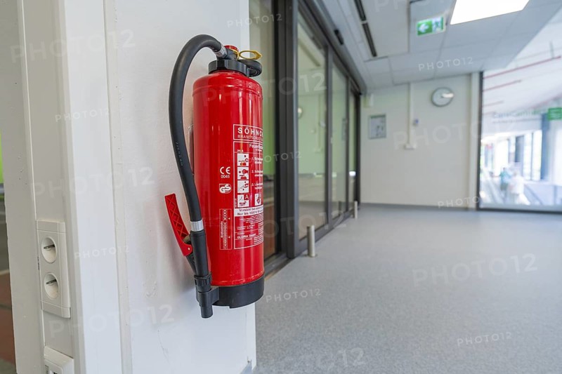Red fire extinguisher on a white wall in the office corridor, Care Connect, vaccination kiosk for refugees, Calw, Germany
