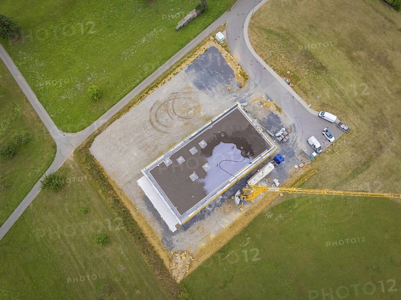 Aerial view of a construction site area with vehicles and a crane next to a partially completed building, green roof, house construction, climate neutral