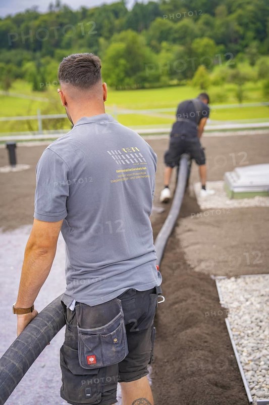 Two construction workers lay a hose on a roof with a view of the surrounding nature, roof greening, house construction, climate neutral