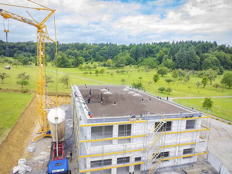 A building under construction with a crane and surrounding landscape, green roof, house construction, climate neutral