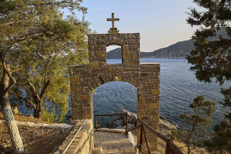 Legend, crab, shell fisherman, stone arch with cross in front of a coastal view of the sea and trees, chapel, small church, Agia Kavouradena Monastery, Xirokambos, Leros, Dodecanese, Greek Islands, Greece